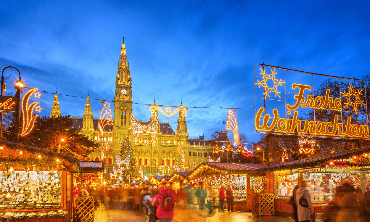 Weihnachtsmarkt vor dem hell erleuchteten Wiener Rathaus bei Dämmerung, mit geschmückten Buden und Leuchtschrift Frohe Weihnachten Weihnachtsmarkt vor dem hell erleuchteten Wiener Rathaus bei Dämmerung, mit geschmückten Buden und Leuchtschrift Frohe Weihnachten